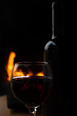 Wine, full wine glass and wine bottle on rustic wooden surface with fire in the background, low key image, dark background, selective focus.