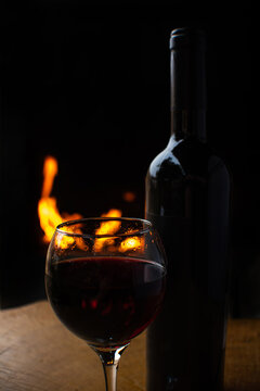 Wine, full wine glass and wine bottle on rustic wooden surface with fire in the background, low key image, dark background, selective focus.