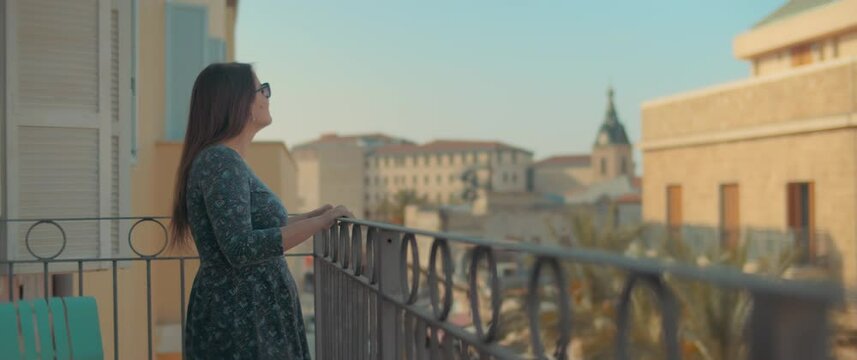 A Beautiful Young Woman Standing At The Balcony And Looking Down The Old European City, Enjoying Her Holiday. Travel, European Summer Vacation. Slow Motion, Handheld.