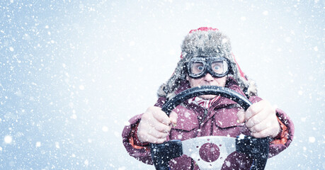 Driving man in red winter clothes and stylish goggles holds a steering wheel, around the snow. 