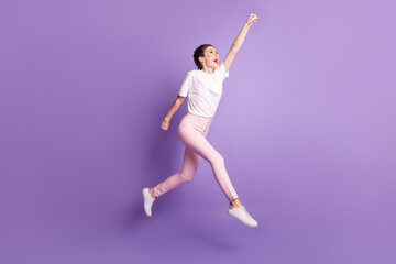 Fototapeta na wymiar Full length photo of excited carefree girl raise hand fist look up empty space isolated on violet color background