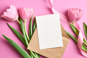 Greeting card mockup with envelope and tulip flowers with ribbon on pink background