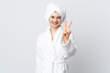 Teenager girl in a bathrobe isolated on white background smiling and showing victory sign