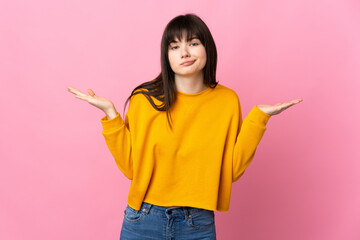 Young Ukrainian woman isolated on pink background having doubts while raising hands