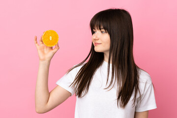 Young Ukrainian woman isolated on pink background holding an orange