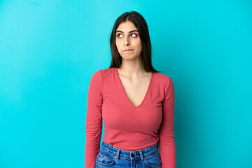 Young caucasian woman isolated on blue background having doubts while looking up