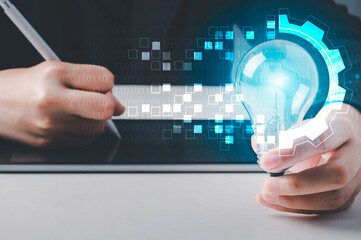 Digital transformation concept. Hand holding light bulb and write on tablet modern interface futuristic blue gear in binary coded background. Connection next generation technology and new era.