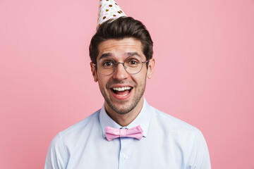 Young white man wearing bow tie and party cone laughing at camera