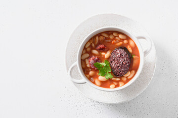 Spanish traditional fabada with haricot, morcilla, tomato paste, chorizo isolated on a white background with copy space. View from above.