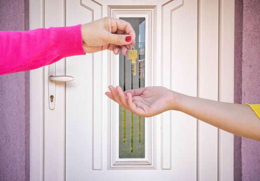 Hand Giving Key To Another Hand In Front Of The Door
