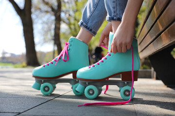 Woman lacing roller skates while sitting on bench outdoors, closeup