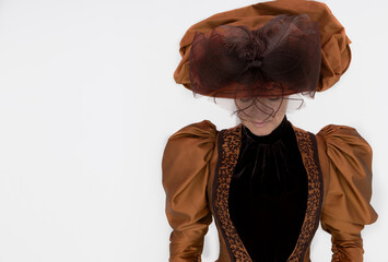 A late Victorian woman wearing a bronze and brown silk ensemble with a large hat 