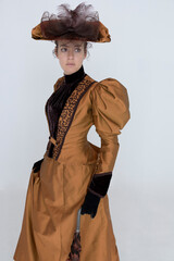 A late Victorian woman wearing a bronze and brown silk ensemble with a large hat 
