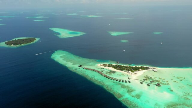 Aerial Panning A Row Of Tropical Island Resort Bungalows Stretching Into Coral Reef Seas With Circles Of Other Reefs Vanishing Into The Distant Horizon - Makunufushi, Maldives