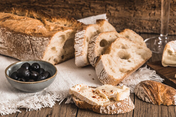 Crusty french white bread with cheese and olives on rustic wooden table