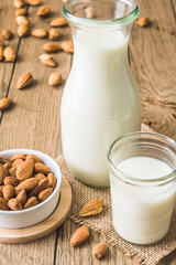 Glass and pitcher with vegan almond milk, almond kernels and whole almonds on an old rustic wooden table, vertical