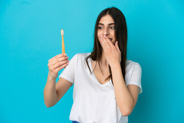 Young caucasian woman brushing teeth isolated on blue background with surprise and shocked facial expression