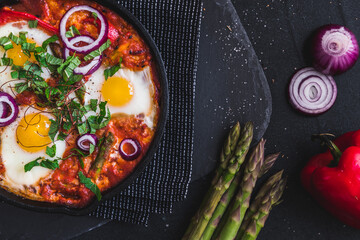 Shakshuka in an iron pan. Middle eastern traditional dish. Fried eggs with tomatoes, bell pepper, vegetables and herbs, sunny side up eggs. Top view.