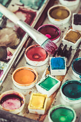 Old paintbox with watercolours. Vibrant colours used on the palette, brush with red paint. Vertical.