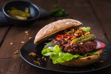 Burger with vegetarian hamburger patty, salad, tomatoes and roasted onions on a black plate on wooden table