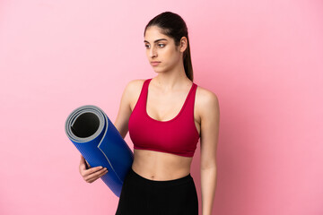 Young sport caucasian woman going to yoga classes while holding a mat looking to the side