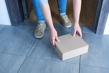 Delivery of parcels to the door. A woman in blue jeans picks up a box with goods delivered by a...