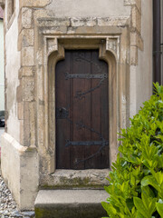 Fototapeta na wymiar Eine Seiteneingangstür aus dunkel-braunen Holz mit schmiedeeisernen Elementen.