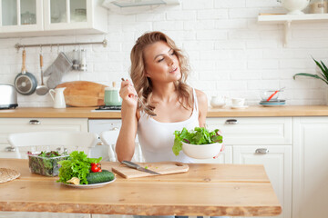 Obraz na płótnie Canvas Young fit woman preparing and eating vegetable salad in her kitchen. Healthy lifestyle and healthy eating concept