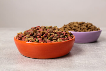 Dry food in pet bowls on grey surface