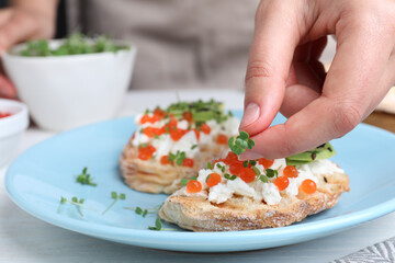 Woman putting microgreens onto sandwich with caviar at table, closeup