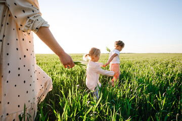 A mother with two daughters is walking in a green field. Hugs and feelings.