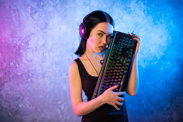 Obraz premium Female esports gamer posing with a gaming gear in neon light. Streamer girl standing with a gaming keyboard.