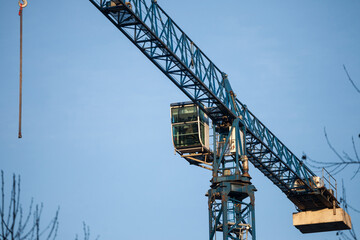 Blue metal crane in front of a building being assembled in a construction site taken from below during a sunny afternoon, under a blue sky...