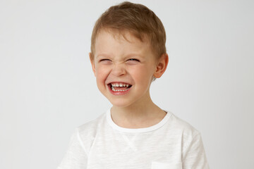 A little boy of preschool age on a white background makes a funny face. The child makes a face