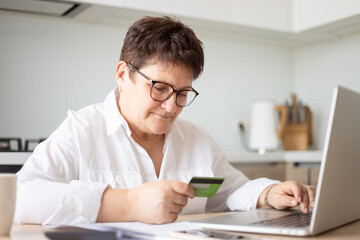 Obraz na płótnie Canvas Mature woman using credit card making online payment at home. Successful old woman doing online shopping using laptop. Closeup of retired lady holding debit card for internet banking account.