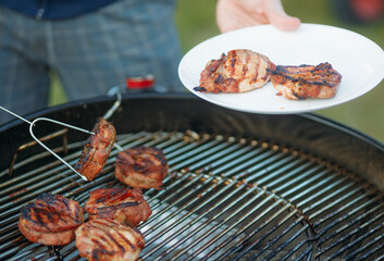 A man prepares steaks on a barbecue grill, outdoors. Picnic on vacation or weekend.