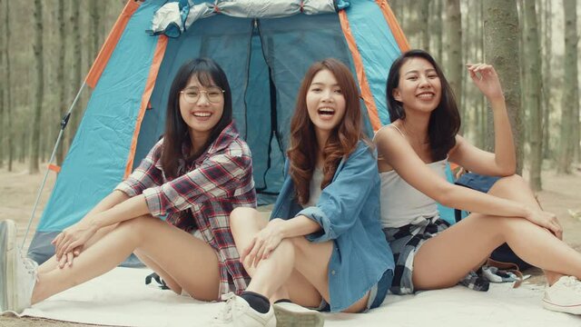 Group of young asia camper friends camping near relax enjoy moment in forest. Female traveler using smartphone taking selfie at campsite. Outdoor activity, adventure travel, or holiday vacation.