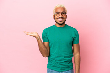 Young Colombian handsome man isolated on pink background holding copyspace imaginary on the palm to...