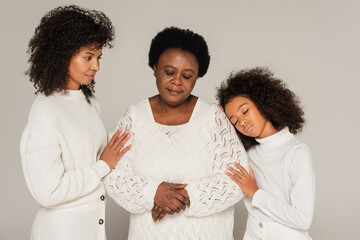 sad african american daughter, mother and granny standing isolated on grey