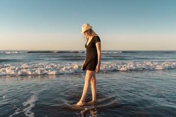 Young woman on the beach at sunset dipping her feet in the water.