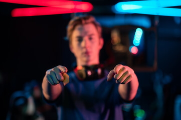 The hands of a young gamer pointing his fingers at the camera, the guy himself in blur © Anna Kosolapova