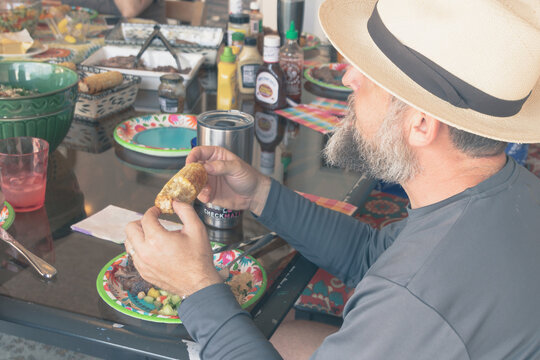 Bearded man with a hat eating Corn on the Cob on a paper plate for dinner