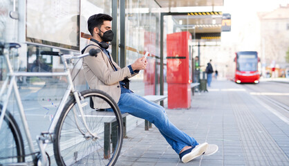 Young business man commuter with smartphone on the way to work outdoors in city, coronavirus concept.
