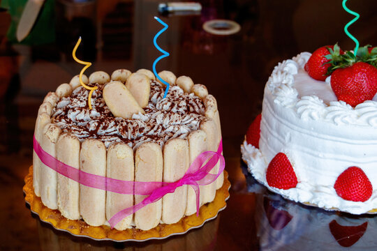 Tiramisu coffee cake with cookies and a pink ribbon holding it together with fonit decorations. Strawberry cheesecake birthday cake with white cream cheese icing an a skinny candle off to right. 
