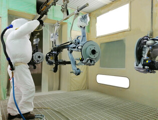 An Asian mechanic is using a car suspension spray gun to prevent rust in the paint room. Specially controlled