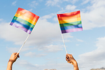 Unrecognizable person hands waving lgbt pride flags with blue sky with clouds in background. Gay Pride's day. activism and human rights.