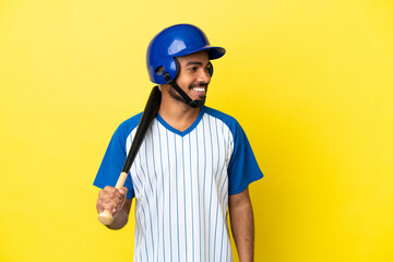 Young Colombian latin man playing baseball isolated on yellow background looking to the side and smiling