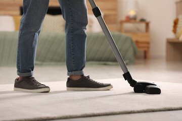 Man cleaning carpet with vacuum cleaner at home, closeup