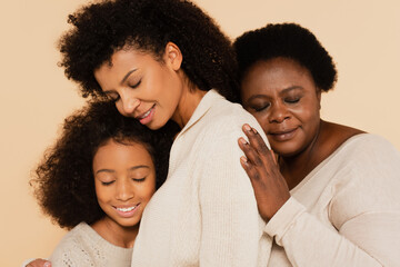 african american grandmother embracing with daughter and granddaughter with closed eyes isolated on beige