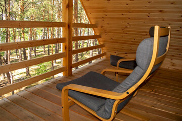 View on a forest from balcony of a modern wooden chalet with two arm chairs. Tourism and summer vacation concept. Summer wooden house in a pine forest, village cottage